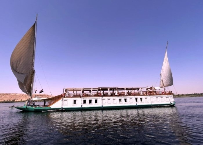Dahabeya Queen Farida sailing on the Nile River with scenic views.