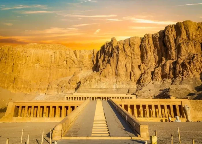 The Mortuary Temple of Hatshepsut at Deir el-Bahari, featuring tiered colonnaded terraces built into massive limestone cliffs near valley of the kings egypt under a golden sunset.
