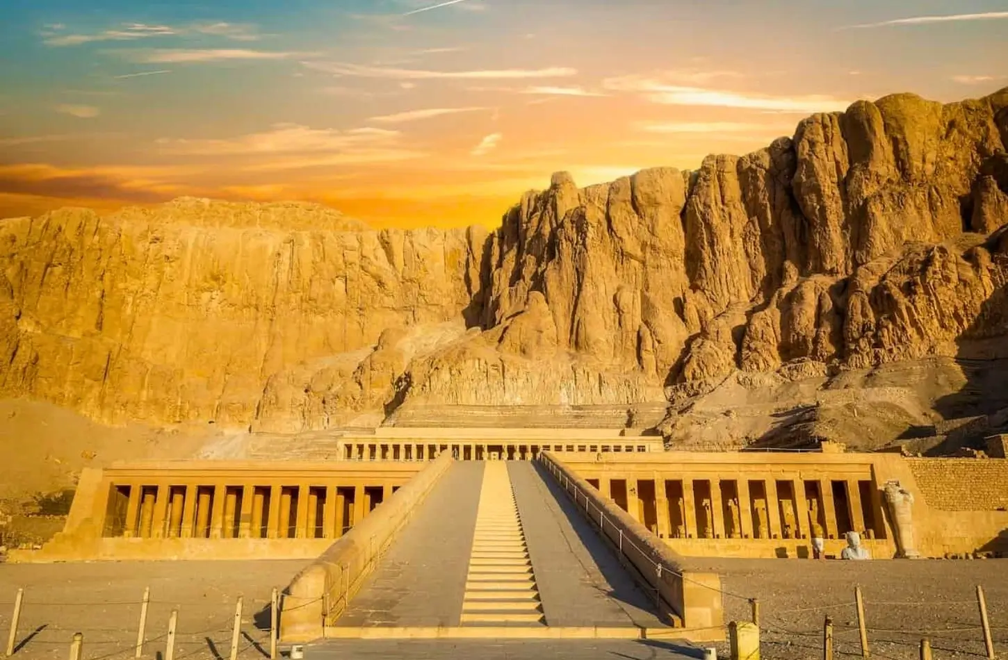 The Mortuary Temple of Hatshepsut at Deir el-Bahari, featuring tiered colonnaded terraces built into massive limestone cliffs near valley of the kings egypt under a golden sunset.