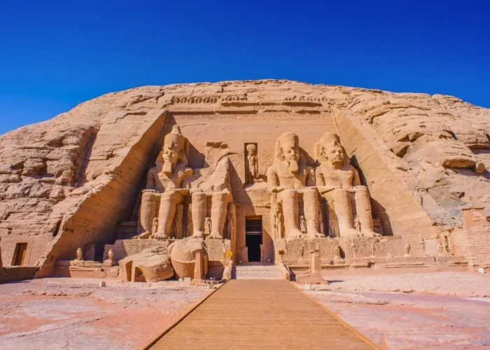 the-Great-abu-simbel-great-temple-ramesses-II-egypt A wide-angle view of the Great Abu Simbel Temple in Egypt, featuring four colossal seated statues of Ramesses II carved into a sandstone cliff under a clear blue sky.